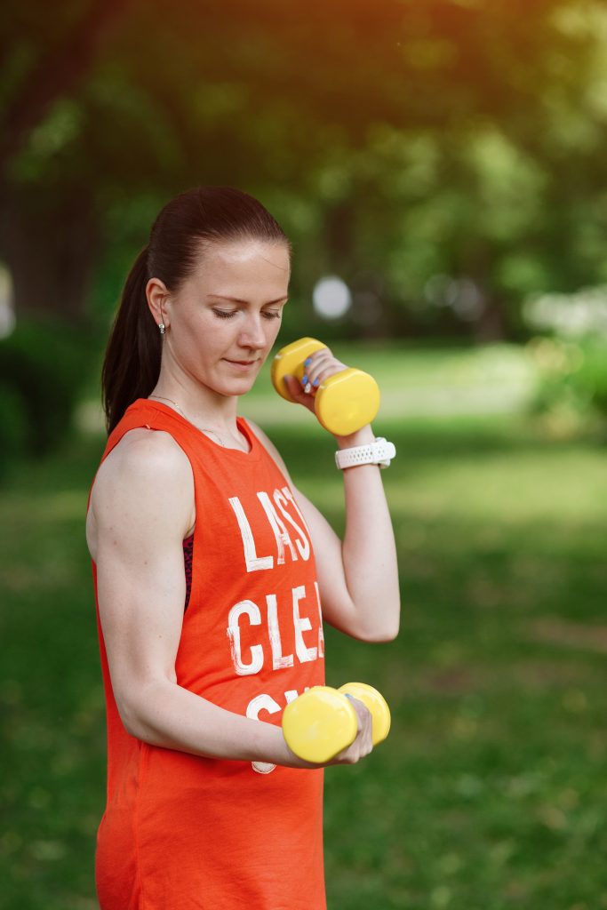 a woman using dumbbells bicep exercise in park